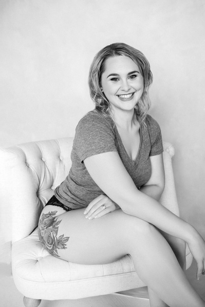 A young woman in a grey t-shirt sits on a swivel chair and smiles at the camera