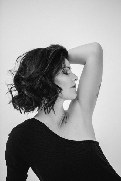 A glamourous brunette woman poses with an arm above her head, face turned towards it