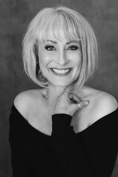 A glamourous older woman with a striking blonde bob beams at the camera