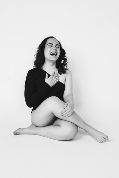 A brunette woman laughs as she sits with one leg crossed over the other