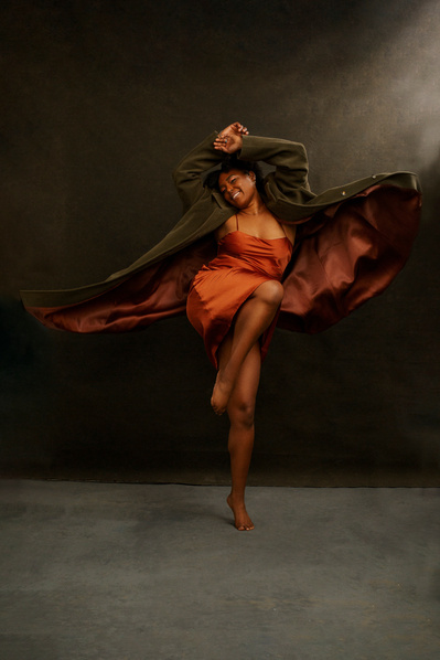 A black woman dances, coat thrown open and away