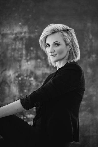 A glamourous blonde woman poses for the camera, hair swept off her face as she looks over her shoulder