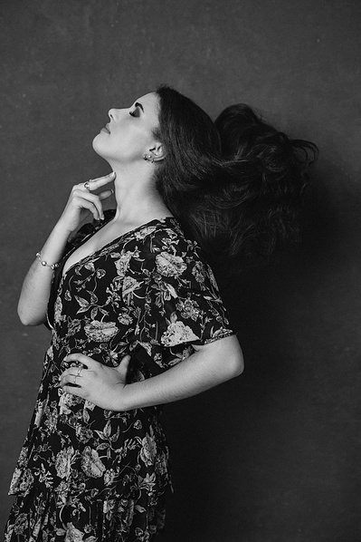A young woman throws back her long brown hair as she touches a finger quizzically to her neck