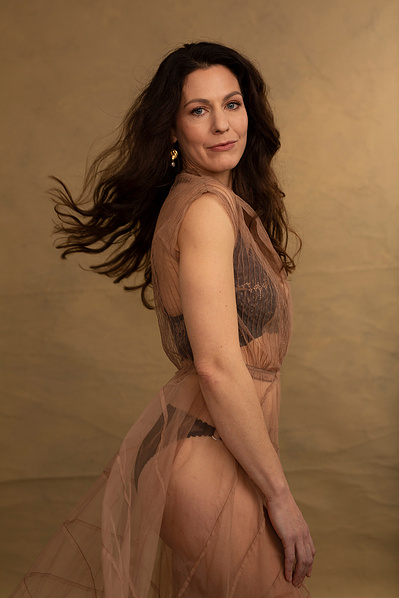 A glamourous woman with long brown hair wears a sheer dress