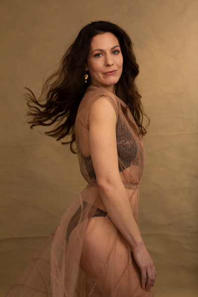 A glamourous woman with long brown hair wears a sheer dress