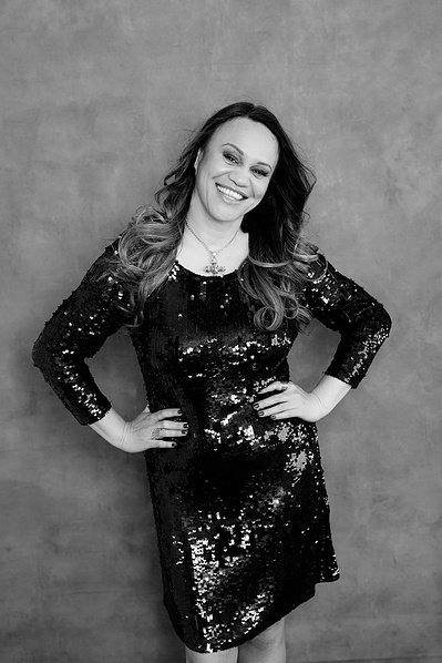 A striking brunette woman wears sequinned dress, hands on hips