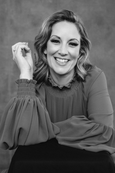 A glamourous blonde woman leans towards the camera and smiles