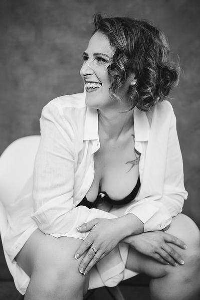 A woman sits in a white chair wearing a white shirt, smiling off camera over her right shoulder