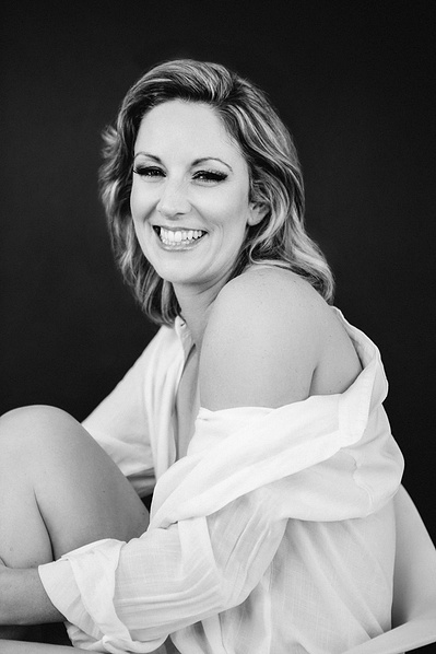 Blonde woman wears a white shirt and smiles at the camera over one shoulder