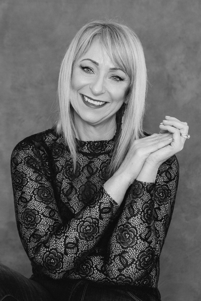 A slim blonde woman smiles at the camera with her head tilted slightly to one side