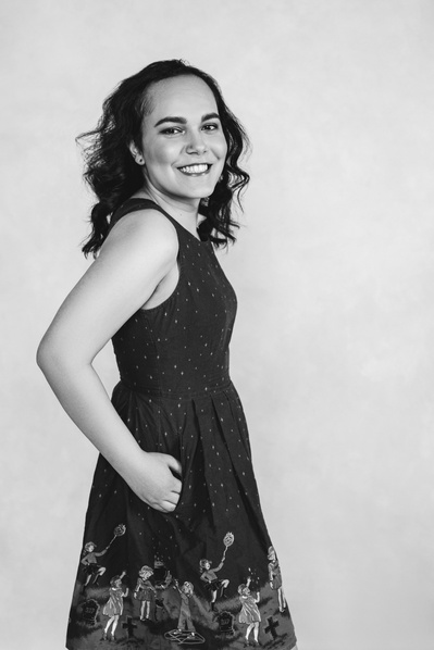 A woman smiles at the camera, she is standing tall and wearing a simple dress