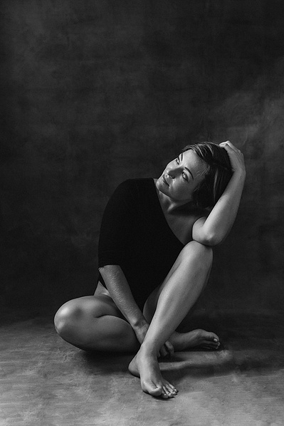 A woman sits, one knee bent up to rest her arm on as she looks off camera