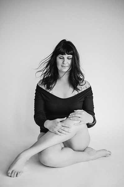 A woman with funky brown hair looks at the ground as she sits with legs crossed