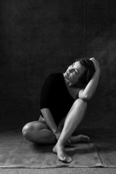 A woman sits on the floor one leg crossed over the other, resting an elbow on a knee
