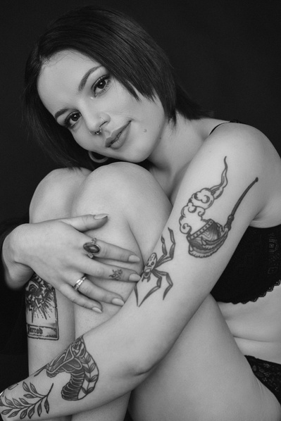 A young woman with tattoos and cropped brown hair sits with arms wrapped around her knees