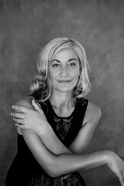 A slim older woman poses for the camera with arms crossed across her torso