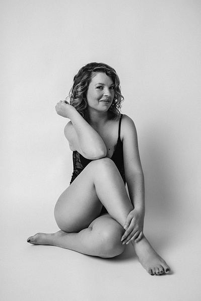 A young woman with curly hair sits with one leg crossed over the other