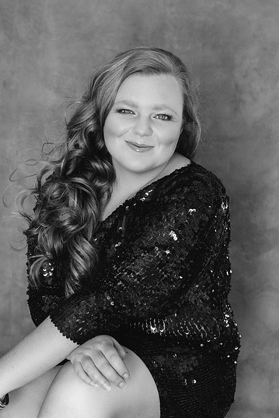 A curly brunette smiles at the camera, arms crossed in front