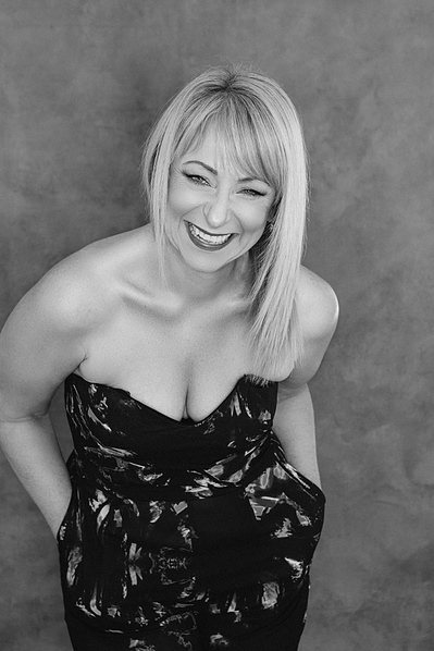 A stylish blonde woman laughs with hands in the pockets of her jumpsuit