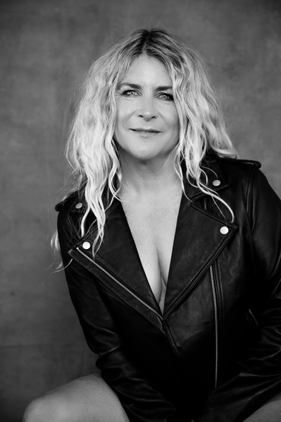 A funky older blonde woman wears a leather jacket, face framed by tousled hair