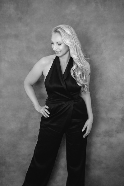 Slim blonde woman wearing a black halter jumpsuit poses with a hand on her hip