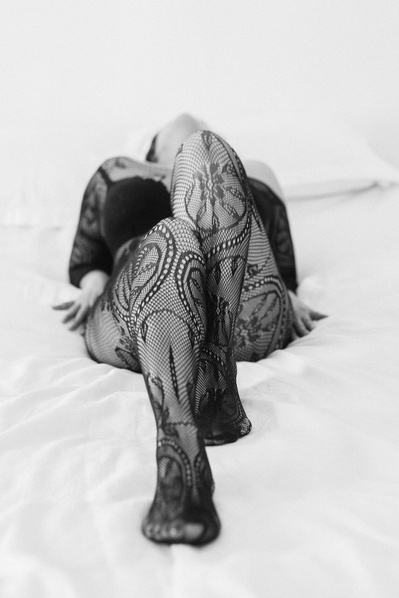 A woman wearing lace bodysuit reclines on the bed, only her legs are clearly visible