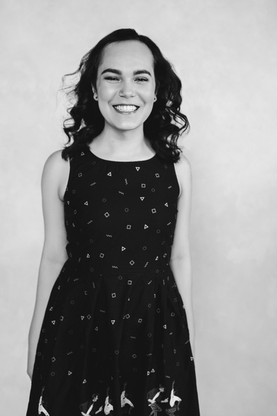 A petite brunette smiles at the camera wearing a simple dress