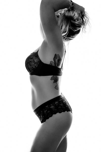 A slim tattooed woman wears underwear and poses with her hands in her hair, face obscured