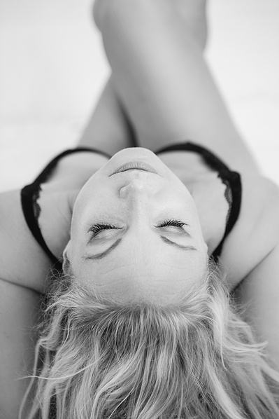A blonde woman reclines on a bed with her head thrown back