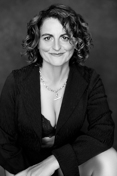 A glamourous older woman wears a black blazer over a bra