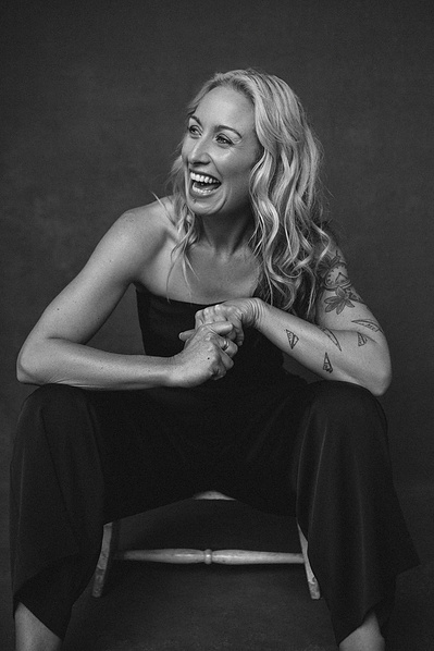 A funky woman with blonde hair sits on a chair as she laughs off camera