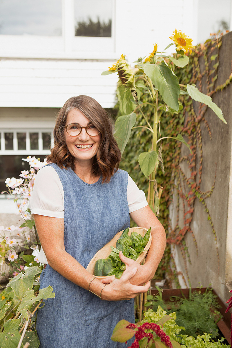 A brunette woman stands in a market garden holding freshly picked produce