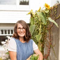 A brunette woman stands in a market garden holding freshly picked produce