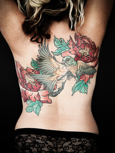 Close up of a woman's back, covered with colourful tattoos