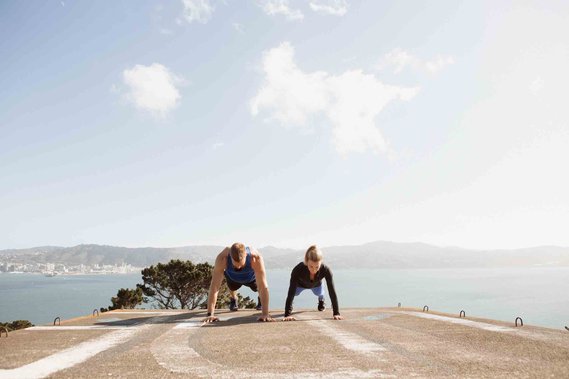 Two personal trainers hold a plank, the cityscape of Wellington visible behind them