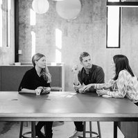 A wide shot of three colleagues having a work meeting, they are seated in a modern office space