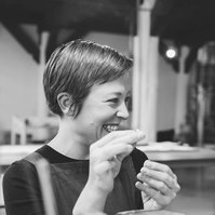 A woman with short brown hair smiles at something off camera as she works on designing a handmade ring