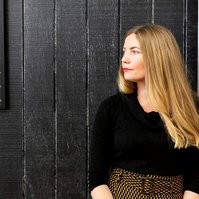 A blonde woman leans against a doorway and looks off camera to her right