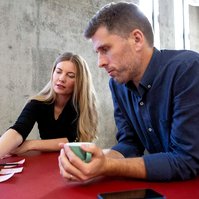 A man and a woman sit at a red table, they are having a work meeting and she is pointing something out