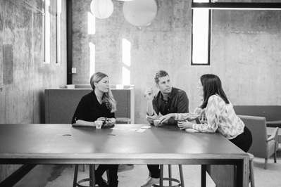 Three people sit around a wooden table for a work meeting