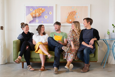 A work team of five people sit on a green sofa smiling at one another