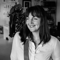 A brunette photographer smiles to the side, her camera strung across her torso