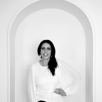 A slim female brunette stands in an archway with one hand on her hip