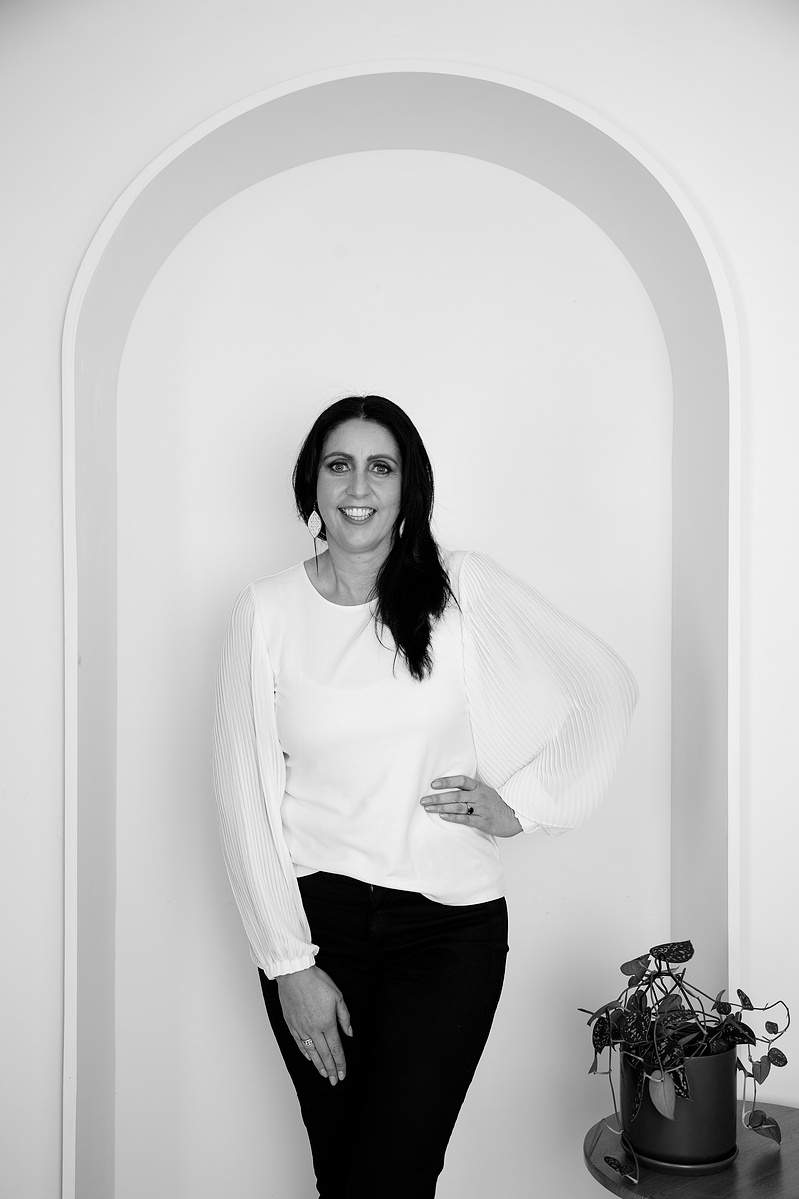 A slim female brunette stands in an archway with one hand on her hip