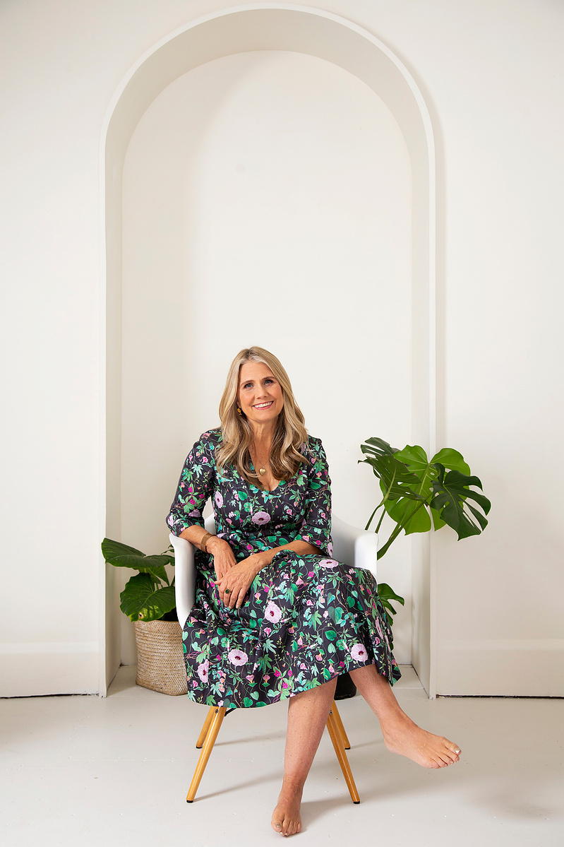 A slim blonde woman sits in a chair in a photography studio