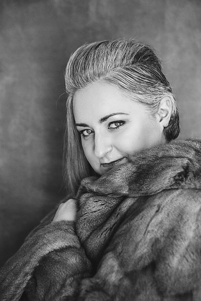 A woman gives a sultry look to the camera from behind a fur coat