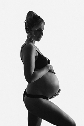 Slim blonde pregnant woman poses in black underwear