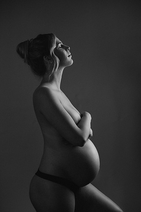 A stunning pregnant woman smiles up at the camera, light framing her curves
