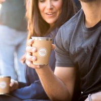A man and a woman enjoy a takeaway coffee on a bus street, their cups are the focus of the photo