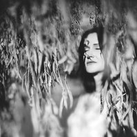 A brunette woman captured in a moment of stillness, she stands against a large tree and her eyes are closed in contemplation